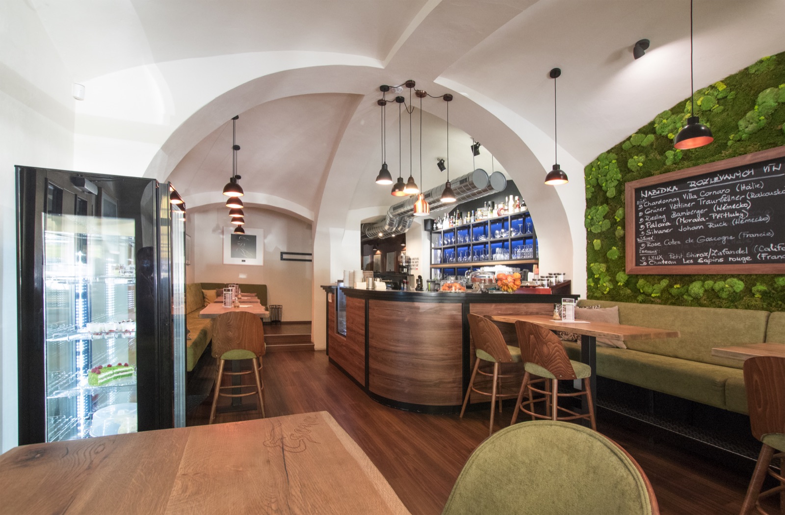 Interiér Esence Café s barem a zelenou mechovou stěnou